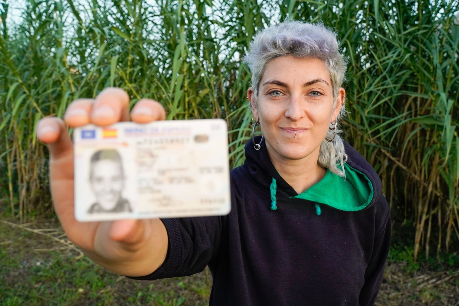 A person outdoors holding up a national identity card bearing their photograph.